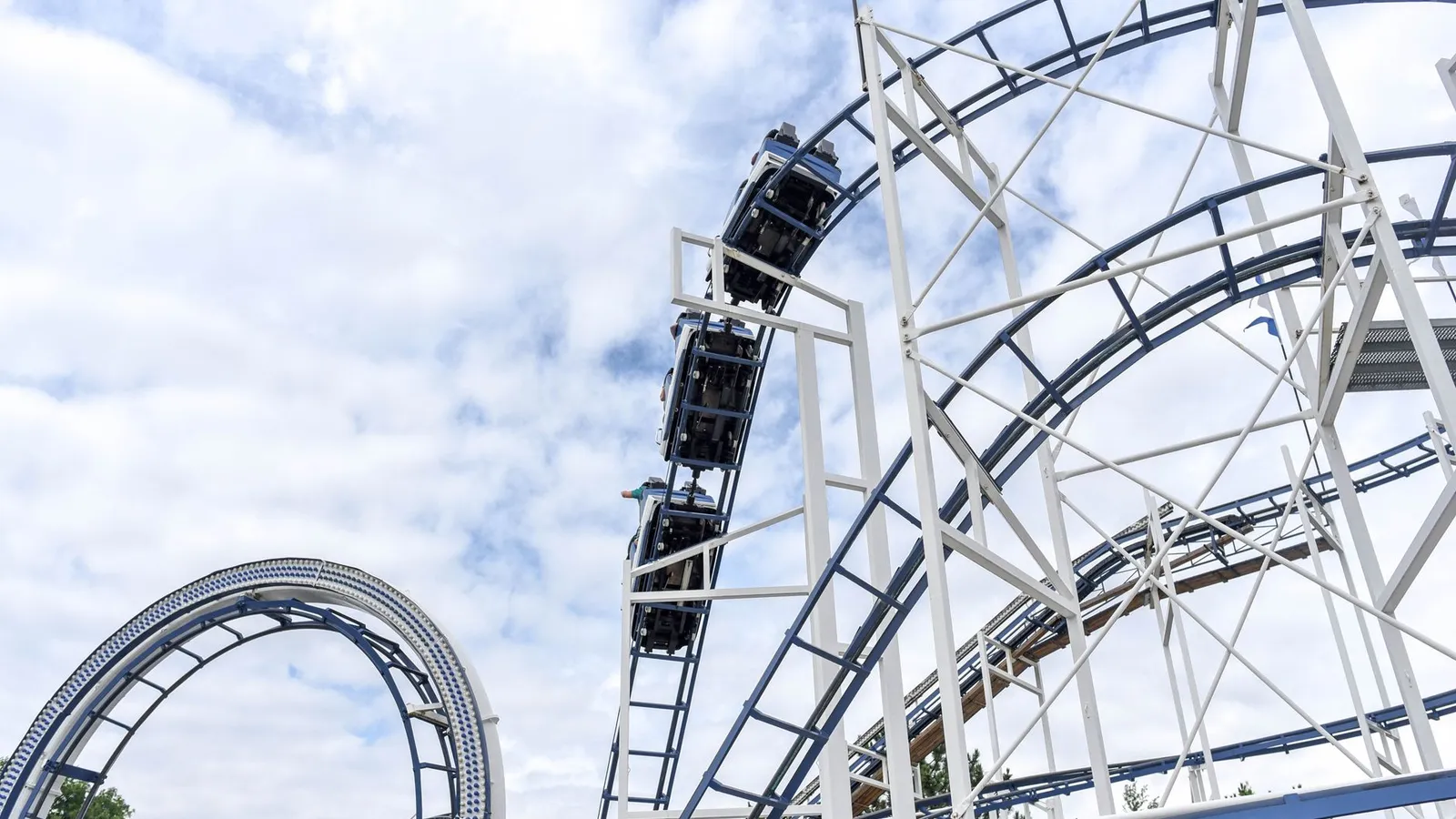 Experience the adrenaline rush of a steel roller coaster under blue skies at an amusement park.