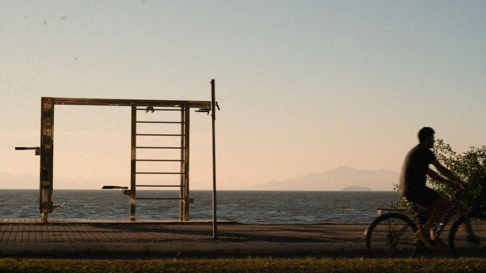 Silhouette of a cyclist riding along a coastal path with mountains in the background at sunset.