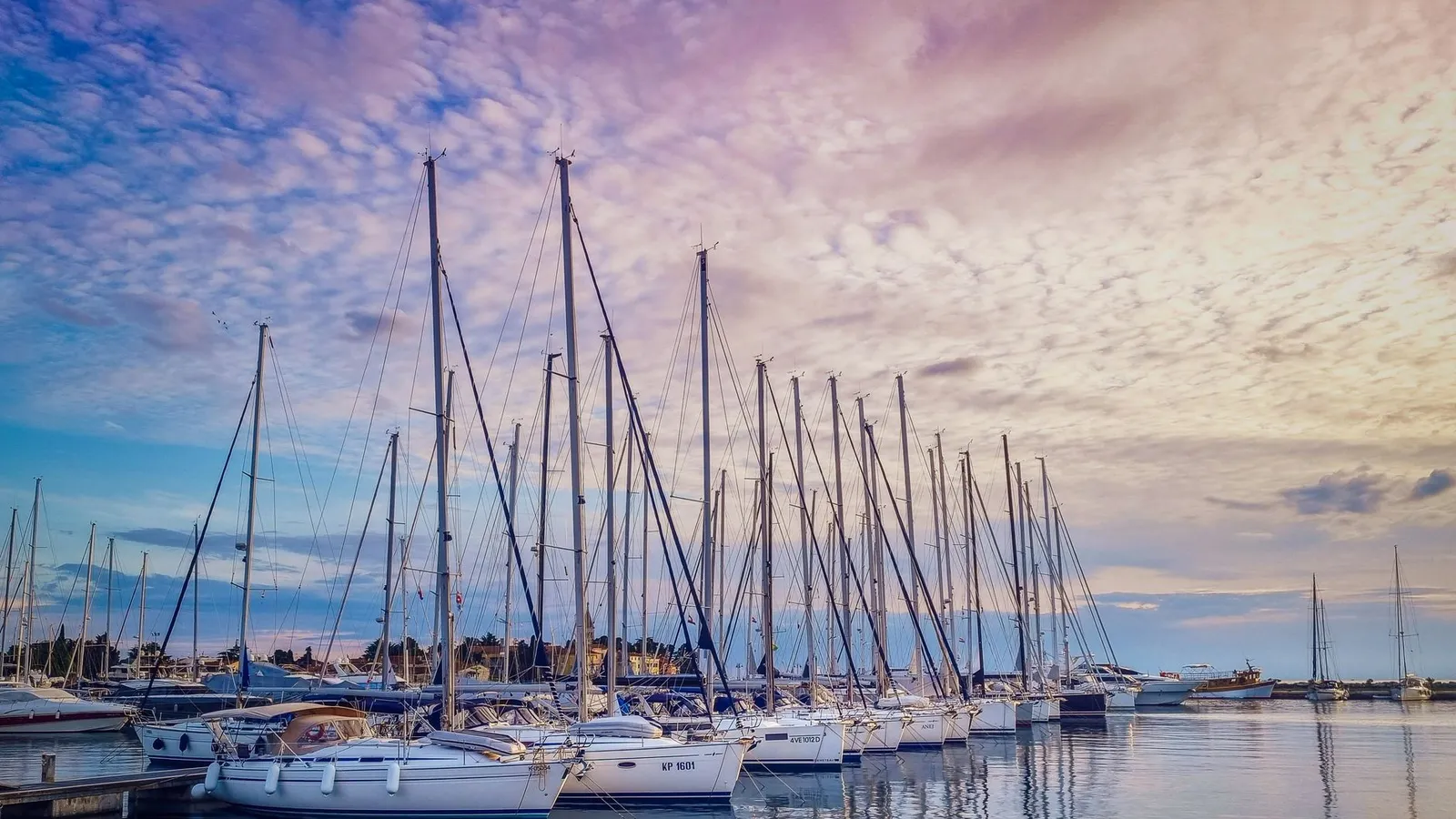Tranquil marina with docked sailboats reflecting on the water at sunset, featuring a colorful sky.