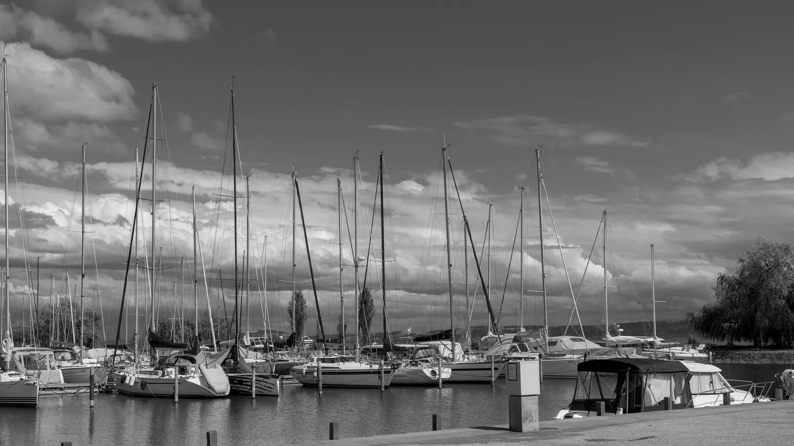 Scenic view of sailboats docked in a marina under a dramatic sky in black and white.