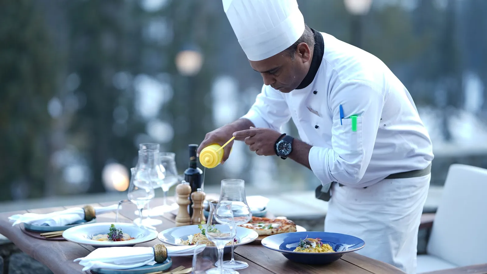A chef skillfully prepares dishes for a stunning outdoor dining experience, showcasing food artistry.
