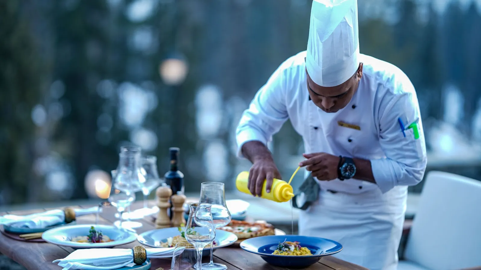Chef expertly adds finishing touches to a gourmet dish at an outdoor restaurant setting.