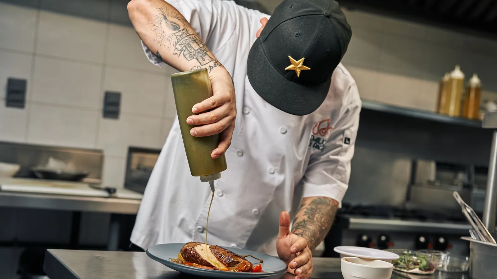 Chef skillfully adds sauce to dish in a professional kitchen setting, showcasing culinary expertise.