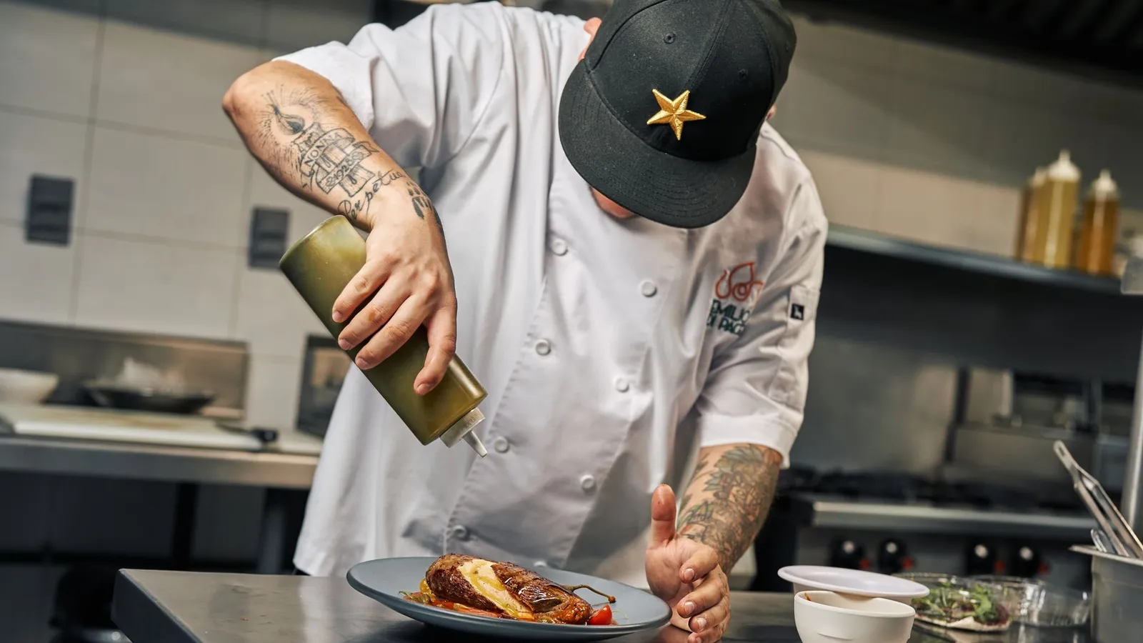 Chef garnishing a gourmet dish with sauce in a professional kitchen setting.