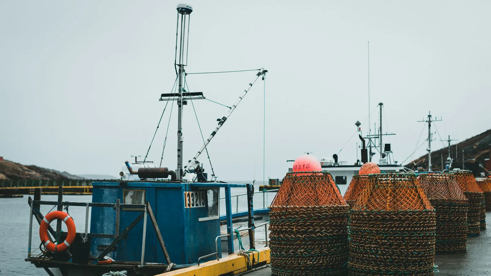 Docked fishing boats with stacked crab pots on a wet harbor under a gray sky.