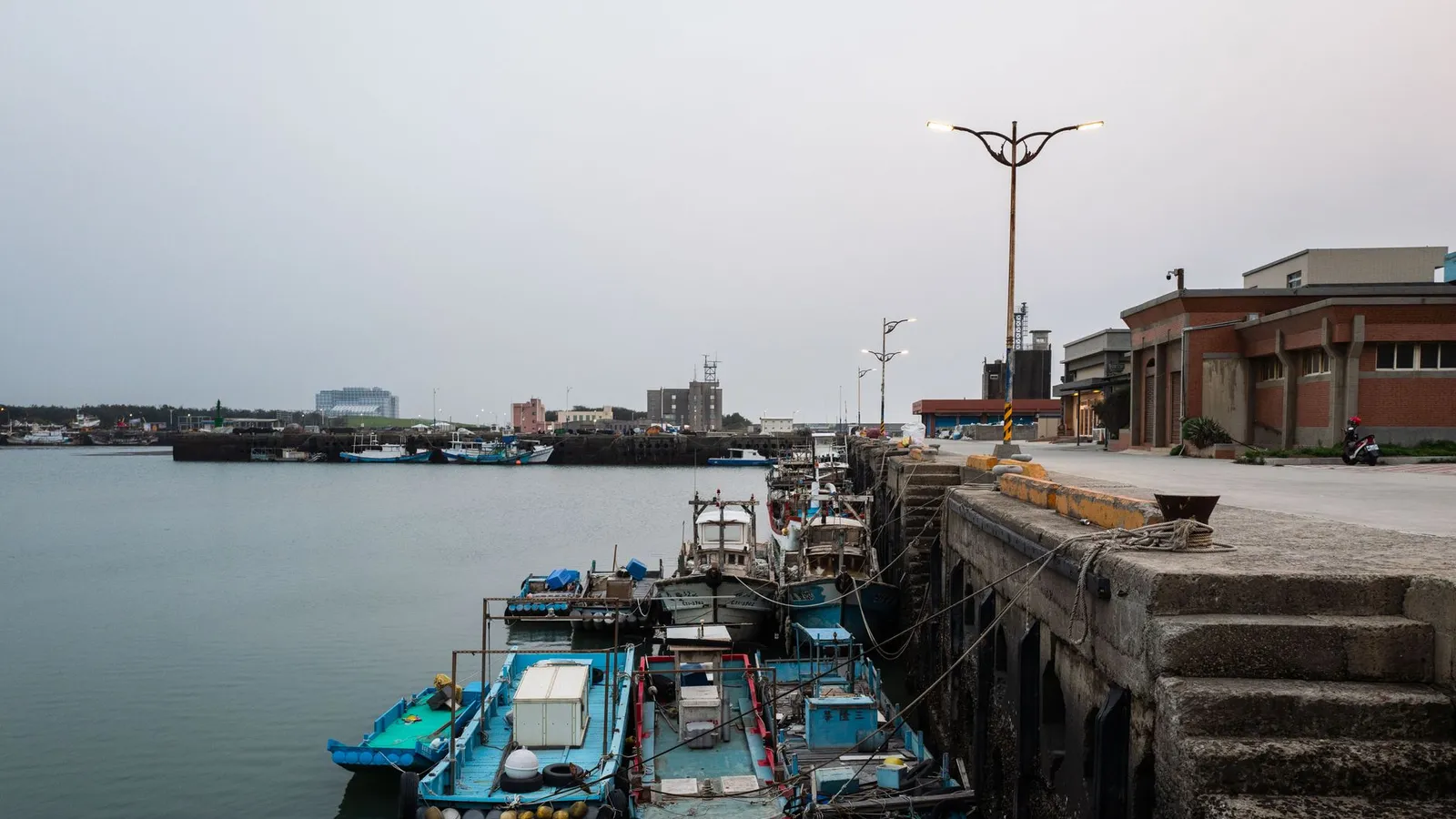 Fishing boats moored at an urban harbor, showcasing a tranquil cityscape at dusk.