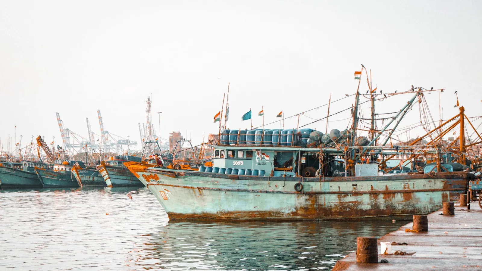 A fleet of rusted fishing boats docked in a bustling harbor under a bright sky.
