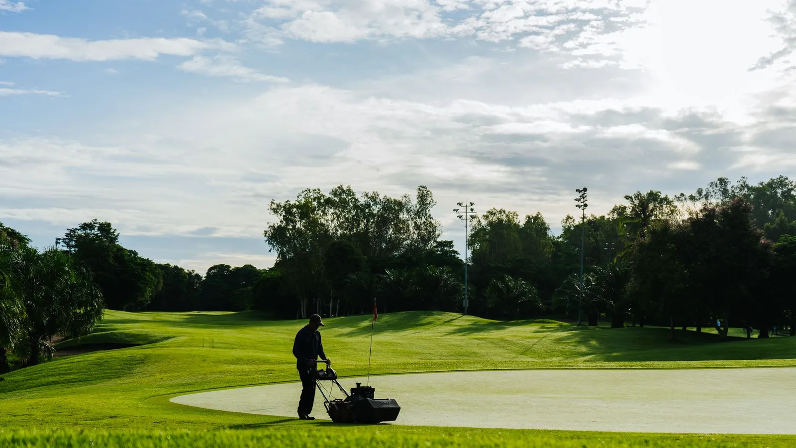 Groundskeeper mowing the green on a golf course during a sunny day, showcasing lush landscapes and maintenance.