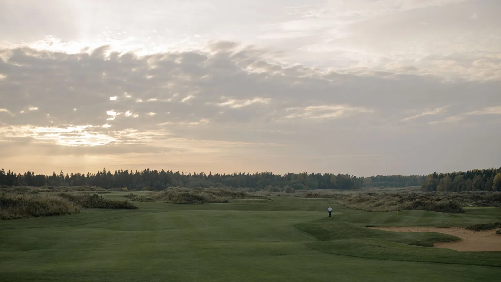 Expansive twilight view of a tranquil golf course with lush greenery under a dramatic sky.