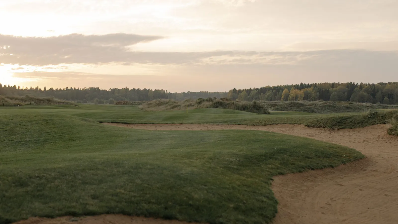 A tranquil golf course landscape at sunset, showcasing green fairways and gentle sandtraps.