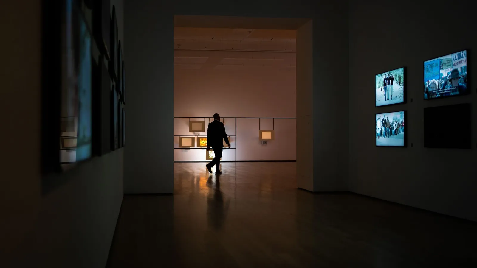 Silhouette of a man walking through a dimly lit art gallery surrounded by illuminated screens.