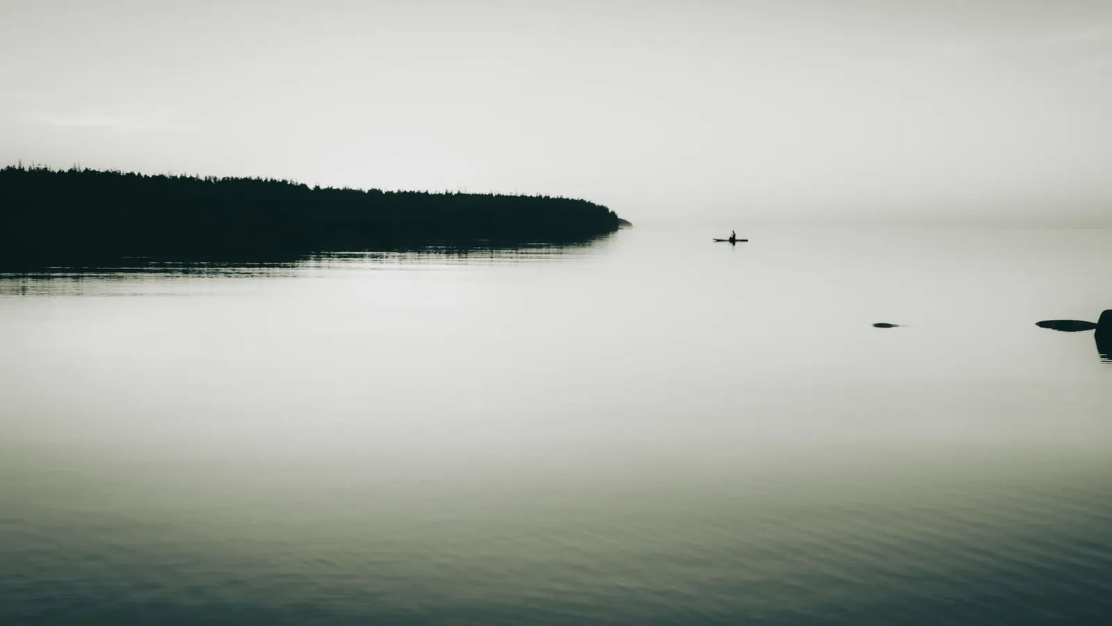 A lone kayaker silhouettes against a serene lake and distant islet at sunset.