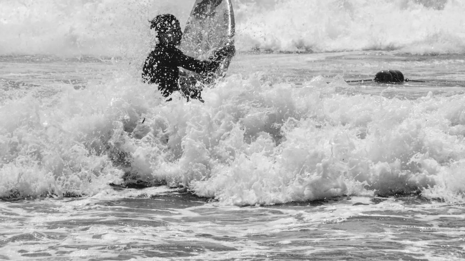A surfer skillfully navigates crashing waves in a monochromatic scene.