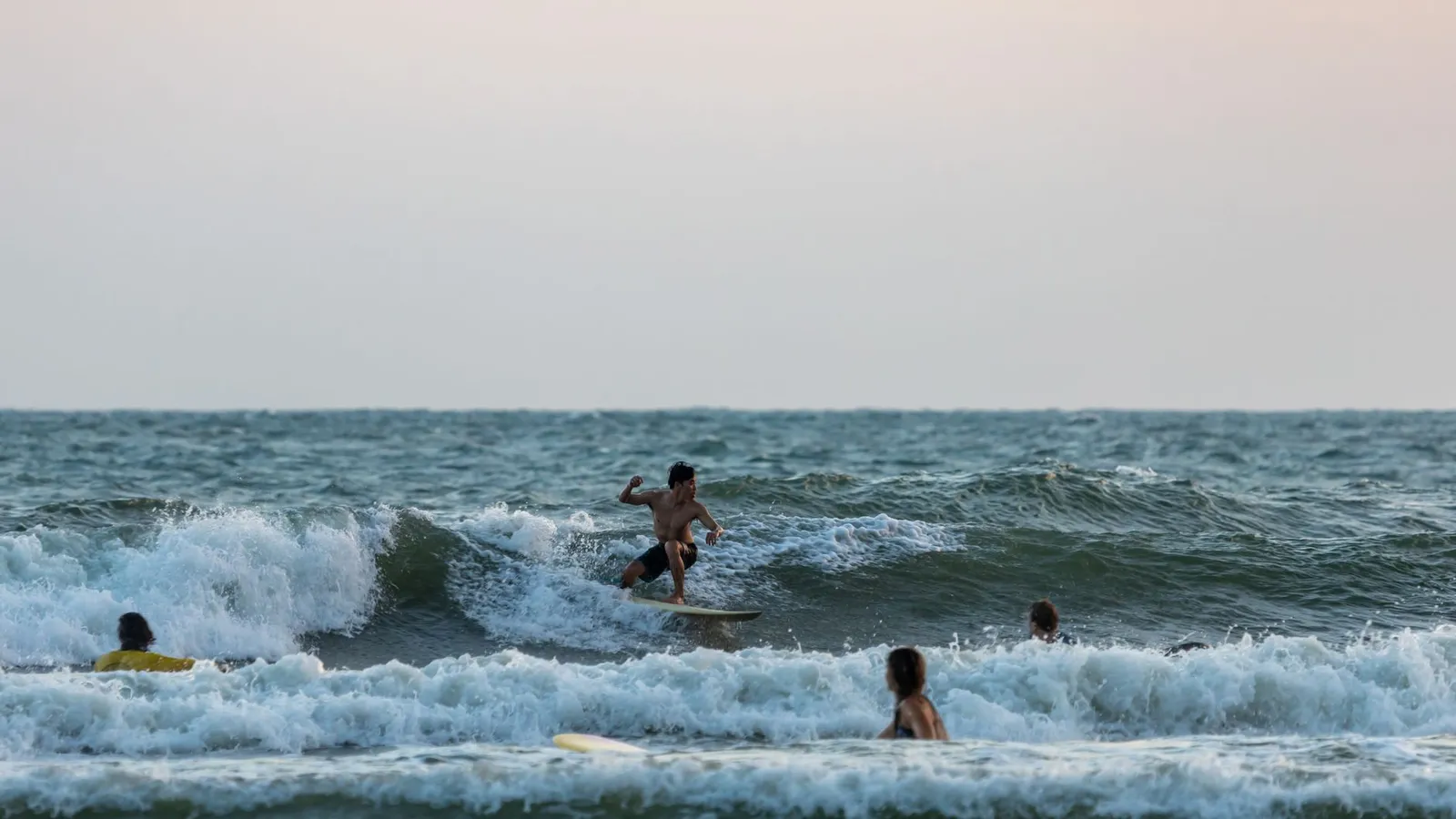 Surfers enjoying the ocean waves as the sun sets, creating a serene seascape.