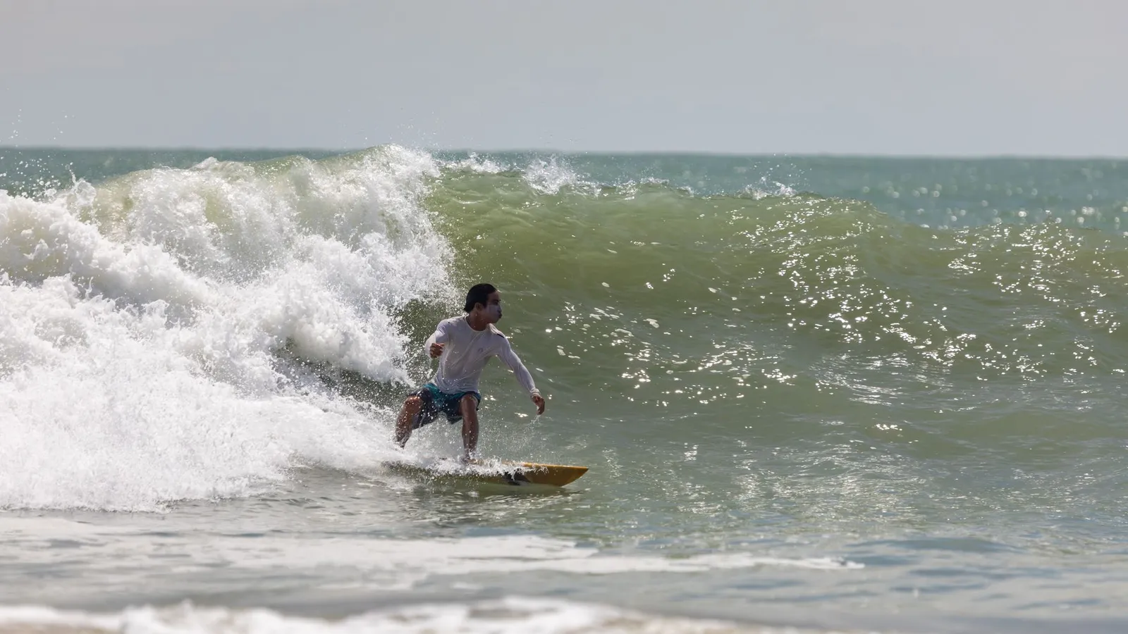 A surfer skillfully navigates a large ocean wave on a sunny day, showcasing surfing expertise.