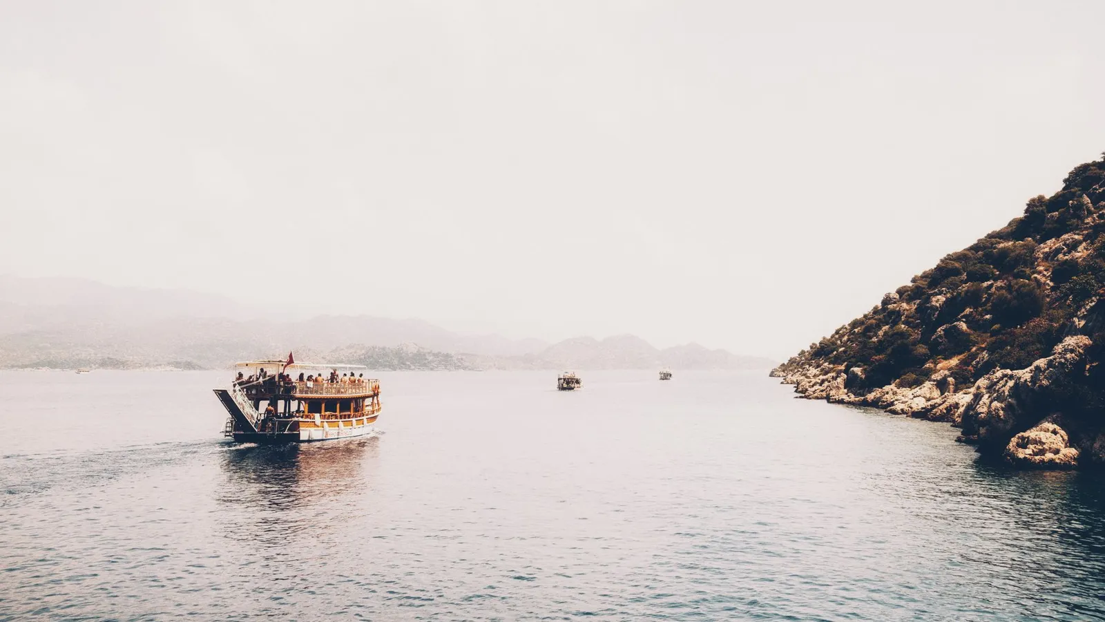 A peaceful boat cruising on a calm sea with a distant coastline under a bright sky.